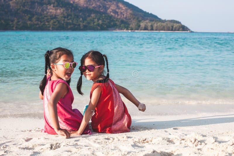 Zwei asiatische kleines Kindermädchen, die zusammen auf dem Strand nahe dem schönen Meer in den Sommerferien sitzen und spielen lizenzfreie stockbilder