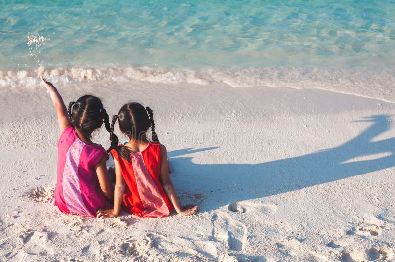 Zwei asiatische kleines Kindermädchen, die zusammen auf dem Strand nahe dem schönen Meer in den Sommerferien sitzen und spielen lizenzfreie stockfotos