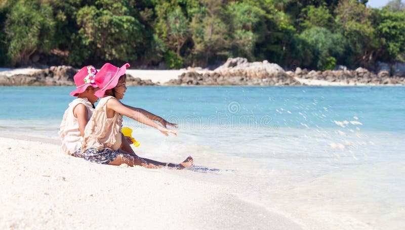 Zwei asiatische kleines Kinderm? dchen, die zusammen mit Sand auf dem Strand nahe dem sch? nen Meer in den Sommerferien sitzen und lizenzfreie stockfotografie