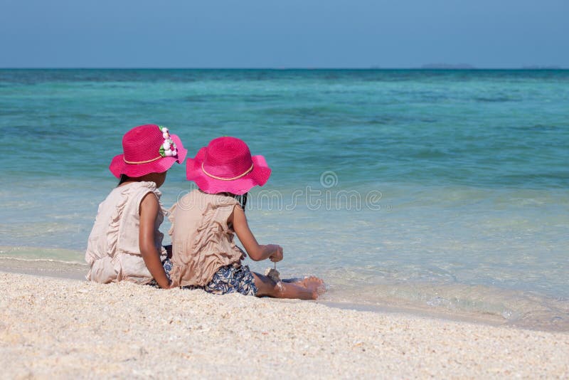 Zwei asiatische kleines Kinderm? dchen, die zusammen mit Sand auf dem Strand nahe dem sch? nen Meer in den Sommerferien sitzen und lizenzfreie stockfotografie