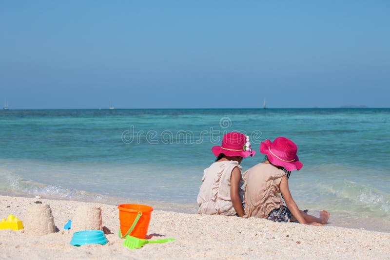 Zwei asiatische kleines Kinderm? dchen, die zusammen mit Sand auf dem Strand nahe dem sch? nen Meer in den Sommerferien sitzen und stockbild