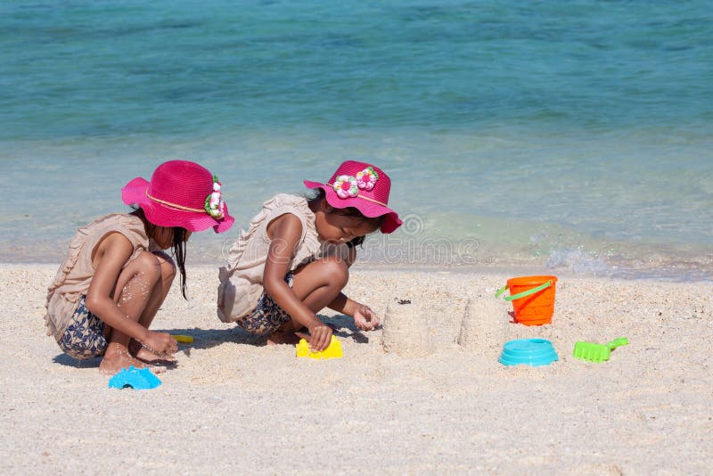 Zwei asiatische kleines Kinderm? dchen, die zusammen mit Sand auf dem Strand nahe dem sch? nen Meer in den Sommerferien sitzen und lizenzfreies stockbild