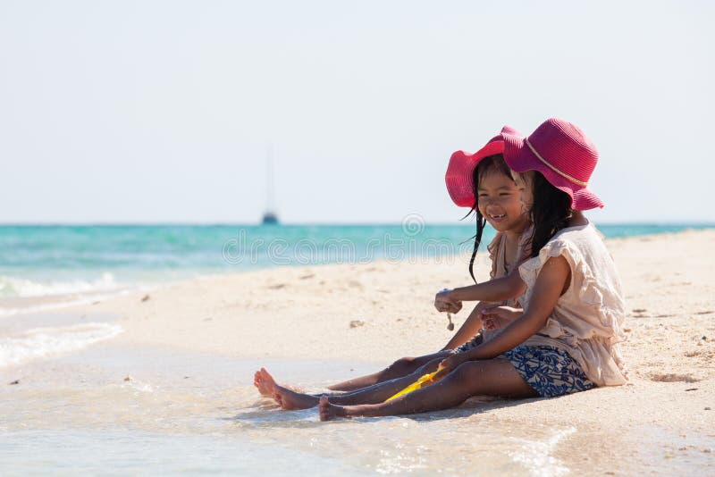Zwei asiatische kleines Kinderm? dchen, die zusammen mit Sand auf dem Strand nahe dem sch? nen Meer in den Sommerferien sitzen und lizenzfreie stockfotografie