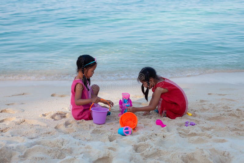 Zwei asiatische kleines Kinderm? dchen, die zusammen mit Sand auf dem Strand nahe dem sch? nen Meer in den Sommerferien sitzen und lizenzfreie stockbilder