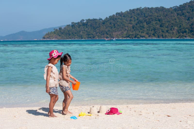 Zwei asiatische kleines Kindermädchen, die zusammen mit Sand auf dem Strand nahe dem schönen Meer in den Sommerferien spielen lizenzfreies stockbild