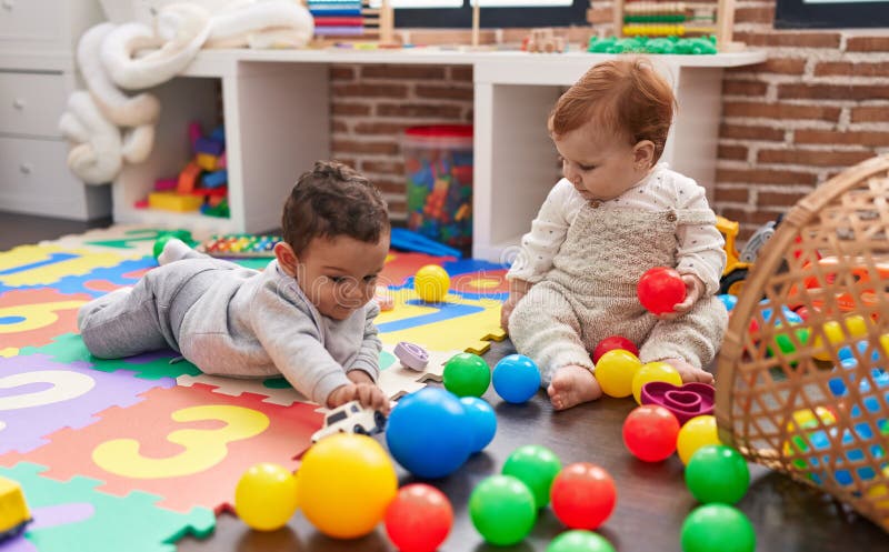 Zwei bezaubernde Babys, die mit Kugeln spielen, die im Kindergarten auf dem Boden sitzen