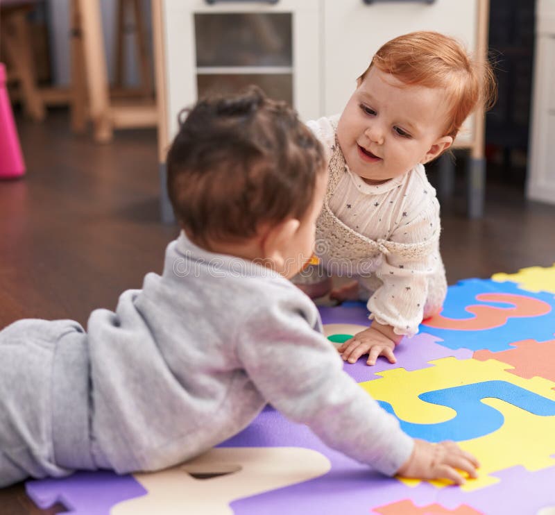 Zwei bezaubernde Babys, die zuversichtlich im Kindergarten auf dem Boden liegen