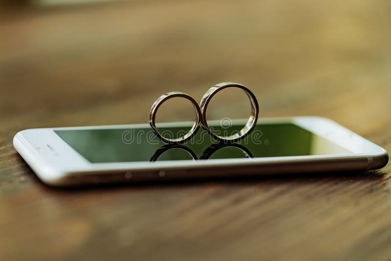 Zwei Eheringe in Form einer Tabelle acht sind am Telefon im Raum Sie werden auf dem Hintergrund des Schirmes angezeigt lizenzfreies stockbild Zwei Eheringe in Form einer Tabelle acht sind am Telefon im Raum Sie werden auf dem Hintergrund des Schirmes angezeigt lizenzfreies stockbild