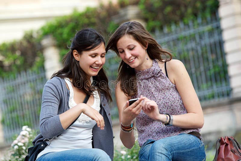 Zwei Einkaufenmädchen im Park mit einem Handy stockbild Zwei Einkaufenmädchen im Park mit einem Handy stockbild