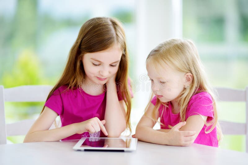 Zwei entzückende kleine Schwestern, die mit einer digitalen Tablette spielen stockfotos Zwei entzückende kleine Schwestern, die mit einer digitalen Tablette spielen stockfotos