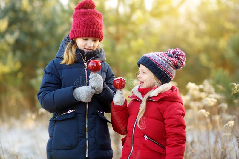 Zwei entzückende Schwestern, welche die roten Äpfel bedeckt mit Zuckerzuckerglasur am schönen sonnigen Weihnachtstag essen stockbilder Zwei entzückende Schwestern, welche die roten Äpfel bedeckt mit Zuckerzuckerglasur am schönen sonnigen Weihnachtstag essen stockbilder