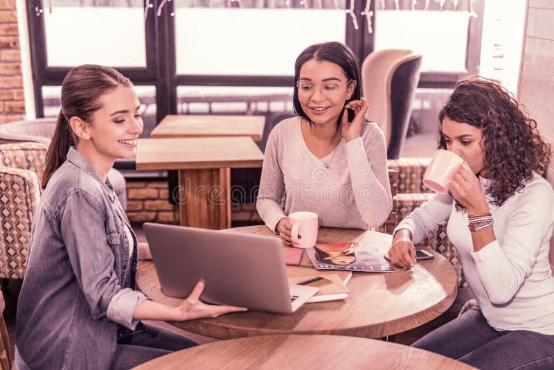 Zwei Frauen, die Tee beim Aufpassen von Darstellung ihres Kollegen auf Laptop trinken lizenzfreie stockfotografie Zwei Frauen, die Tee beim Aufpassen von Darstellung ihres Kollegen auf Laptop trinken lizenzfreie stockfotografie