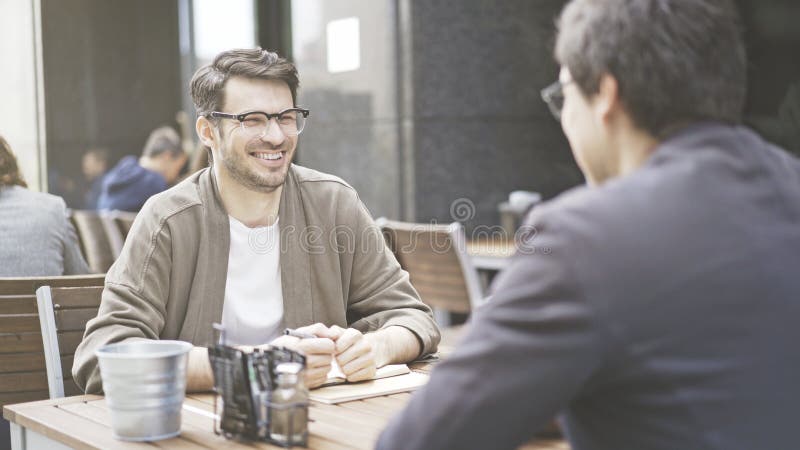 Zwei Freunde lachen bei Tisch vom Café draußen lizenzfreie stockbilder Zwei Freunde lachen bei Tisch vom Café draußen lizenzfreie stockbilder