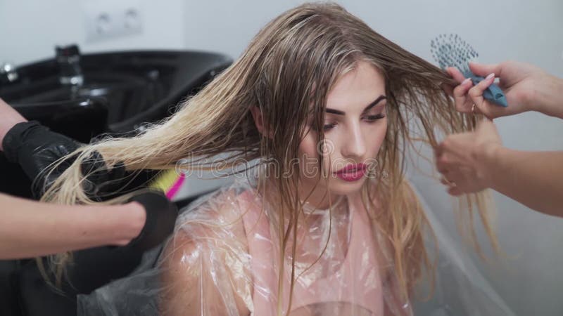 Zwei Friseure kämmen Frau lange nasse blonde Haare nach Färbeverfahren