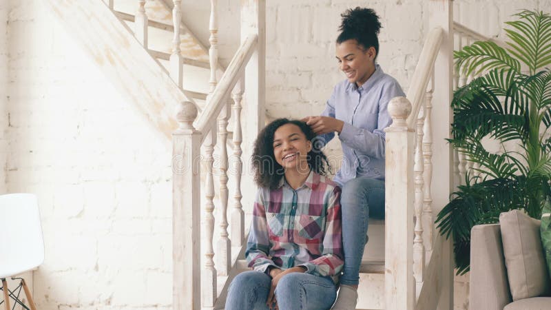 Zwei gelockte Mädchenschwestern des Afroamerikaners machen Spaß gelockte Frisur und haben Spaß zu Hause