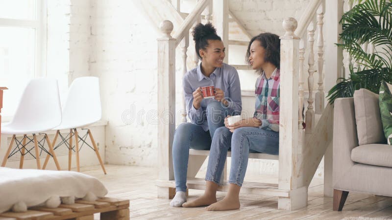 Zwei gelockte sistres Mädchen des Afroamerikaners, die auf Treppe sitzen, haben den Spaß, der zusammen lacht und zu Hause plauder