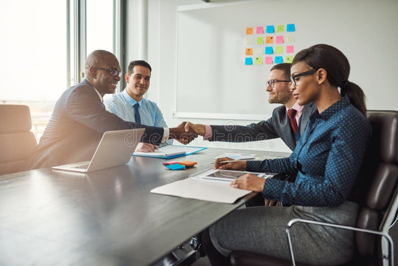 Two young multiracial business teams reaching an agreement in negotiations stretch across the table in the conference room to shake hands. Two young multiracial business teams reaching an agreement in negotiations stretch across the table in the conference room to shake hands