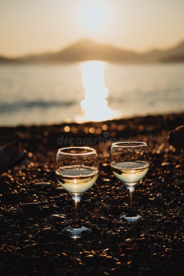 Zwei Gläser mit Weißwein auf dem Strand bei Sonnenuntergang stockbild Zwei Gläser mit Weißwein auf dem Strand bei Sonnenuntergang stockbild