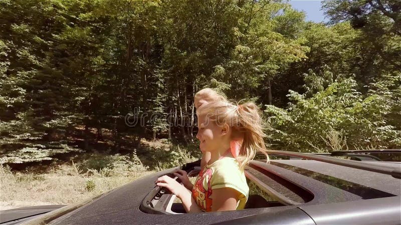 Zwei glückliche junge Blondinen, die das Springen aus Luke des Autos heraus in Bewegung gegen den Wald lachen