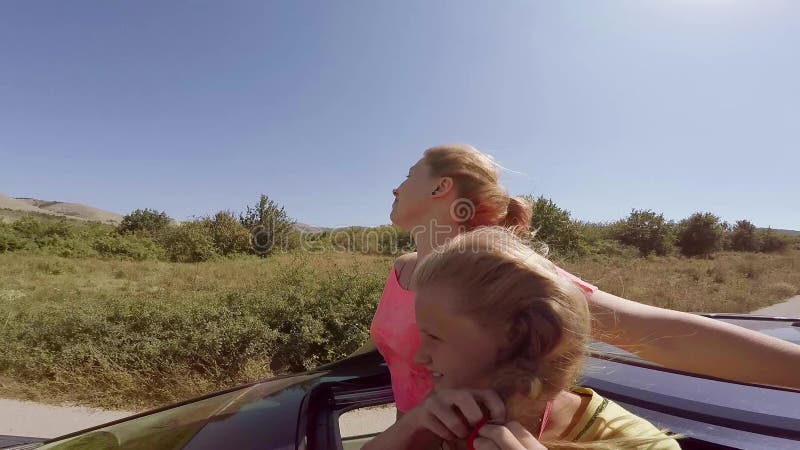 Zwei glückliche junge Blondinen, die das Springen aus Luke des Autos heraus in Bewegung gegen den Wald lachen