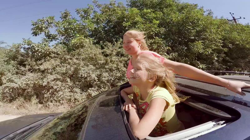 Zwei glückliche junge Blondinen, die das Springen aus Luke des Autos heraus in Bewegung gegen den Wald lachen