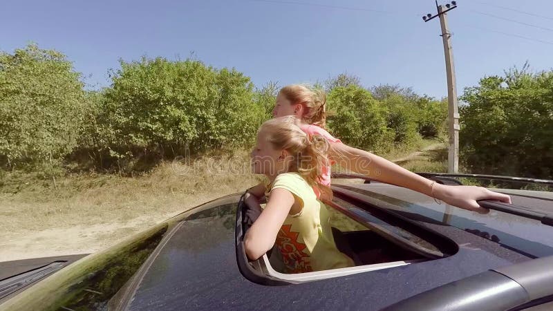 Zwei glückliche junge Blondinen, die das Springen aus Luke des Autos heraus in Bewegung gegen den Wald lachen