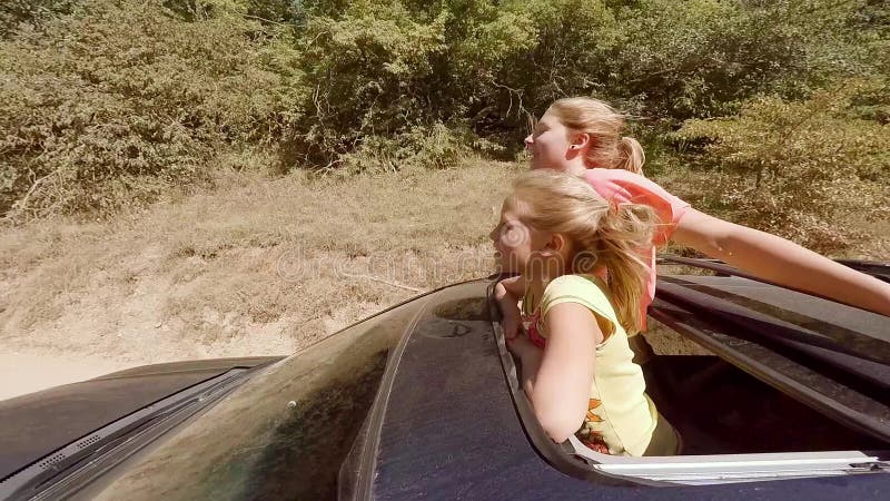 Zwei glückliche junge Blondinen, die das Springen aus Luke des Autos heraus in Bewegung gegen den Wald lachen