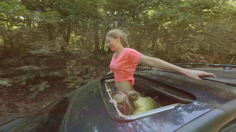 Zwei glückliche junge Blondinen, die das Springen aus Luke des Autos heraus in Bewegung gegen den Wald lachen