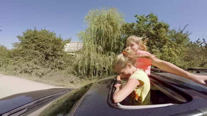 Zwei glückliche junge Blondinen, die das Springen aus Luke des Autos heraus in Bewegung gegen den Wald lachen