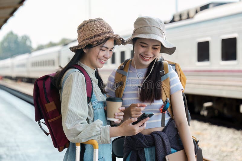Zwei glückliche weibliche Bahnreisende checken am Telefon nach Reiseinformationen und genießen Kaffee stockbild