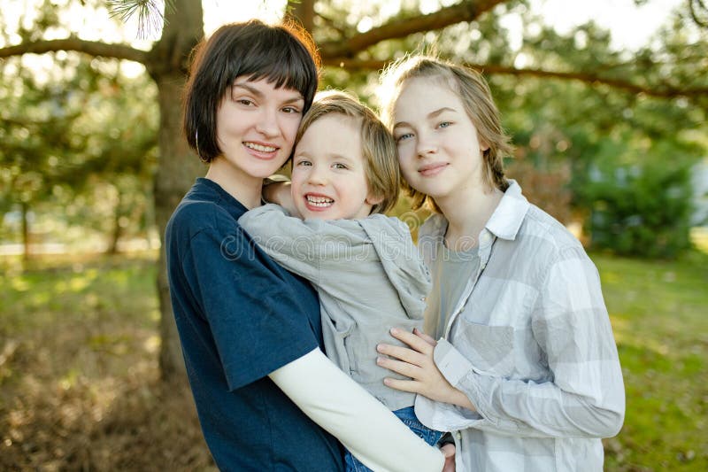 Zwei große Schwestern und ihr kleiner Bruder amüsieren sich draußen. Zwei junge Mädchen mit kleinem Jungen am Frühlingstag. Kinder stockbild
