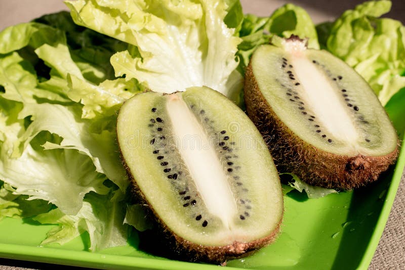 Zwei halbsaftige, reife Kiwi-Früchte, frischer knackiger Salat auf dem Teller Grüner Hintergrund Salatblatt Bio-gesunde Lebensmit stockfoto
