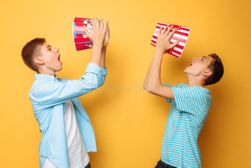 Zwei Jugendliche, die Popcorn essen und Spaß auf einem gelben Hintergrund haben stockfoto Zwei Jugendliche, die Popcorn essen und Spaß auf einem gelben Hintergrund haben stockfoto