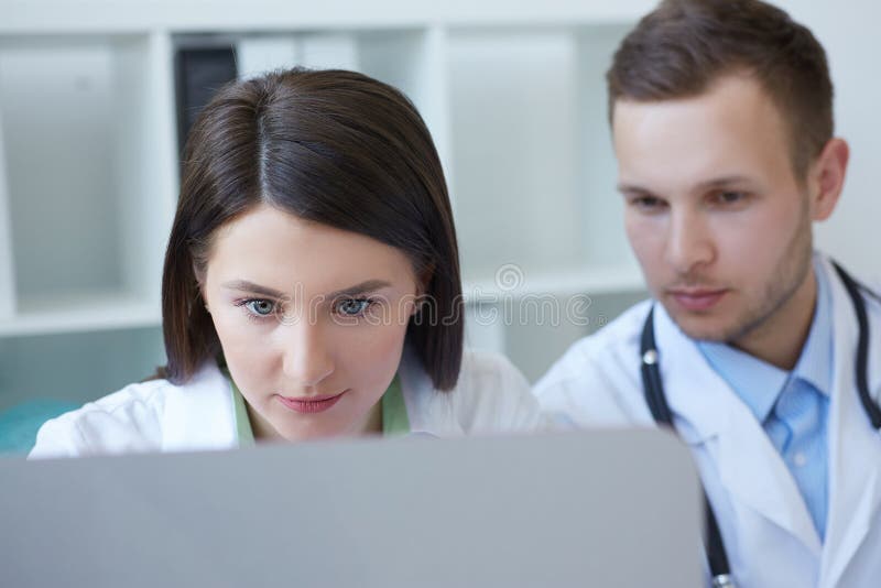 Zwei junge Doktoren, die zusammen neue Weise der Behandlung beim Haben einer Sitzung im Büro besprechen Doktoren, die den Desktop lizenzfreie stockbilder Zwei junge Doktoren, die zusammen neue Weise der Behandlung beim Haben einer Sitzung im Büro besprechen Doktoren, die den Desktop lizenzfreie stockbilder