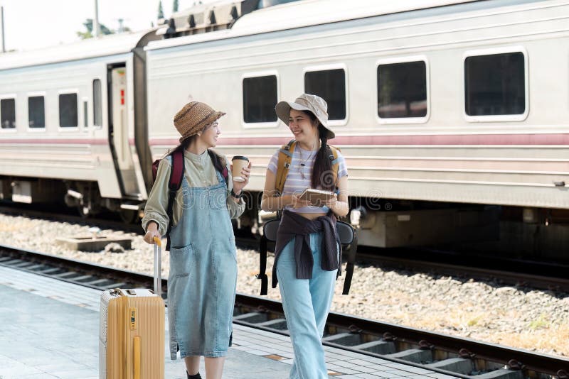 Zwei junge Frauen, die mit dem Zug fahren und am Bahnsteig lächeln und chatten lizenzfreies stockfoto