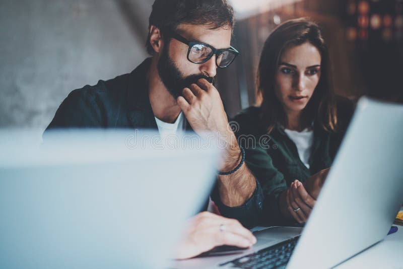 Zwei junge Mitarbeiter, die zusammen an Laptops am modernen coworking Studio nachts arbeiten Tragende Gläser des Mannes unter Ver lizenzfreies stockfoto Zwei junge Mitarbeiter, die zusammen an Laptops am modernen coworking Studio nachts arbeiten Tragende Gläser des Mannes unter Ver lizenzfreies stockfoto