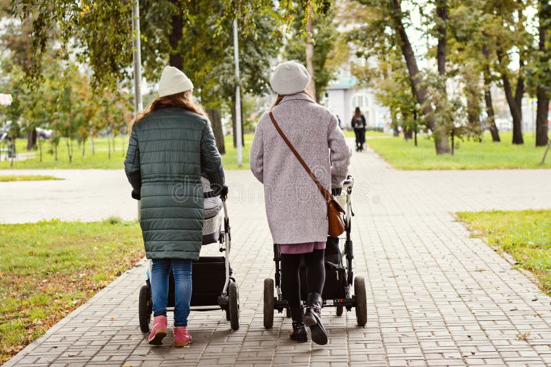 Zwei junge Mutterfreundinnen gehen mit Kleinkindern in den Spaziergängern für einen Herbst Park Frauen auf einem Weg mit den Kind lizenzfreie stockfotografie Zwei junge Mutterfreundinnen gehen mit Kleinkindern in den Spaziergängern für einen Herbst Park Frauen auf einem Weg mit den Kind lizenzfreie stockfotografie