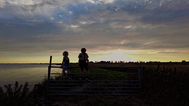 Zwei Jungs, die den schönen, farbenfrohen Sonnenuntergang beobachten stockfoto