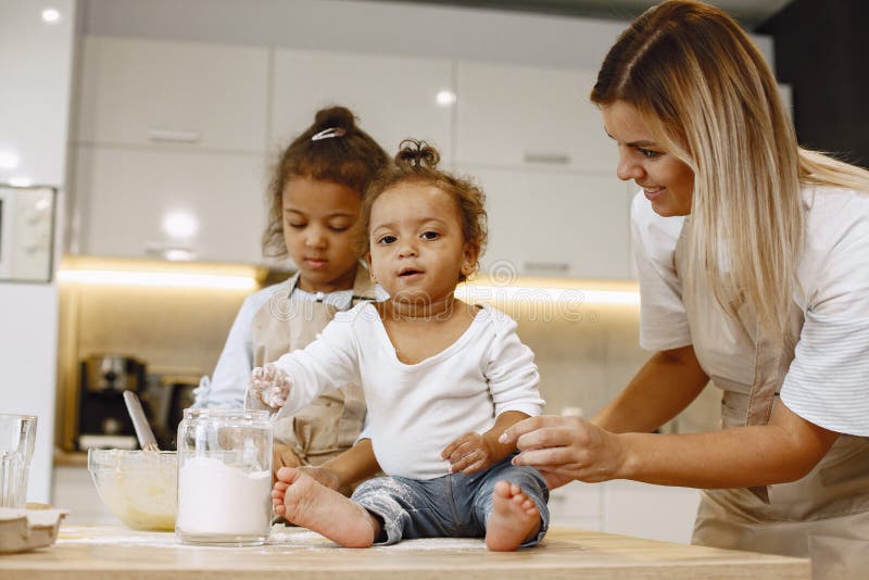 Zwei Kinder in einer Küche mit ihrer Mutter. kleine Mädchen mit Teig. Kind in beige Schürze lizenzfreie stockfotos