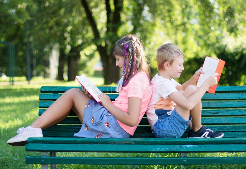 Zwei Kinder sitzen auf der Bank zurück und lesen ein Buch im Park stockfotos