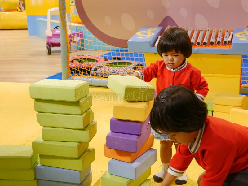 Zwei kleine asiatische Babys, die Schwestern, stapelnd herauf Schaummauerziegel/blockiert zusammen an einem Innenspielplatz lizenzfreie stockfotos Zwei kleine asiatische Babys, die Schwestern, stapelnd herauf Schaummauerziegel/blockiert zusammen an einem Innenspielplatz lizenzfreie stockfotos