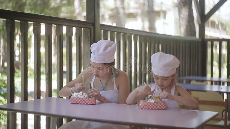 Zwei Kleine Mädchen in Form Von Köchen Sitzen am Tisch Und Essen Die Heißen Kartoffeln, Die Durch Sie Gekocht Werden Stock Footage - Video von familie, kind: 102293600