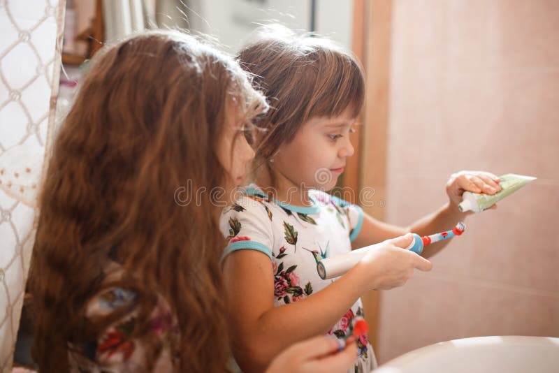 Zwei kleine nette Schwestern, die in den identischen Hemden gekleidet werden, putzen ihre Zähne im Badezimmer stockfotografie Zwei kleine nette Schwestern, die in den identischen Hemden gekleidet werden, putzen ihre Zähne im Badezimmer stockfotografie
