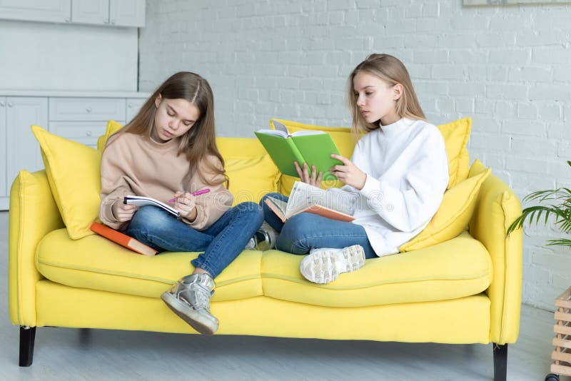 Zwei kleine Schwestern in der zuf?lligen Kleidung, die zusammen auf gelbem Sofa sitzt lizenzfreies stockbild Zwei kleine Schwestern in der zuf?lligen Kleidung, die zusammen auf gelbem Sofa sitzt lizenzfreies stockbild