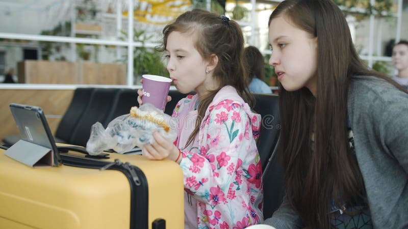 Zwei Mädchen beobachten die Tablette und trinken Tee mit Keksen am Flughafen