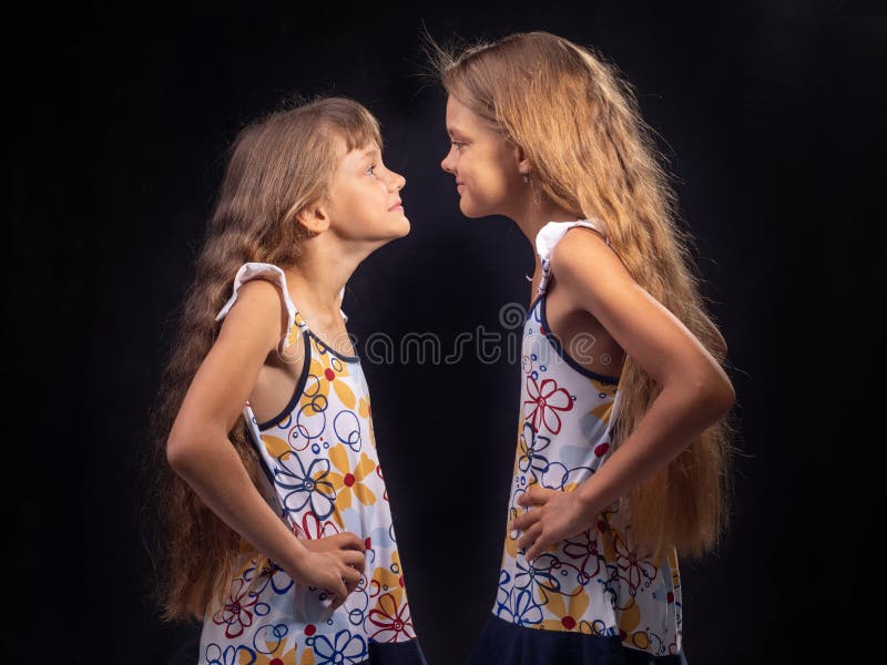 Zwei Mädchen stehen gegenüber von einander und setzend betrachten ihre Hände auf ihre Seiten einander lizenzfreies stockbild Zwei Mädchen stehen gegenüber von einander und setzend betrachten ihre Hände auf ihre Seiten einander lizenzfreies stockbild