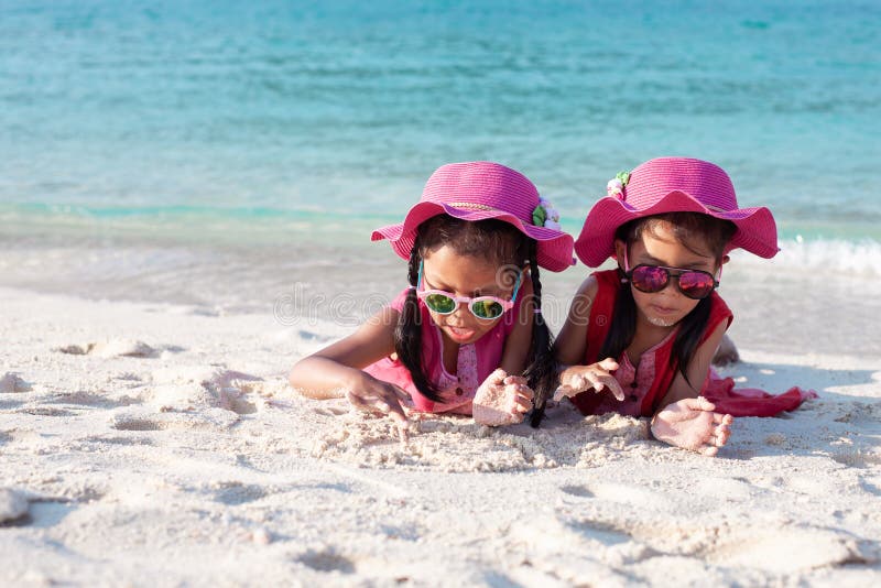 Zwei nette asiatische Kindermädchen, die rosa Hut und die Sonnenbrille zusammen spielt mit Sand auf dem Strand nahe dem schönen lizenzfreie stockfotografie