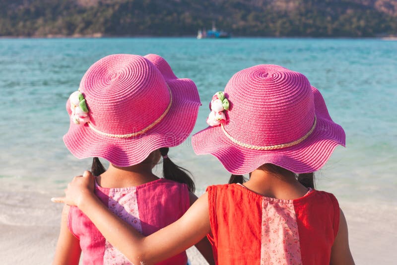 Zwei nette asiatische kleines Kindermädchen, die auf dem Strand nahe dem schönen Meer sitzen und sich umarmen stockbild