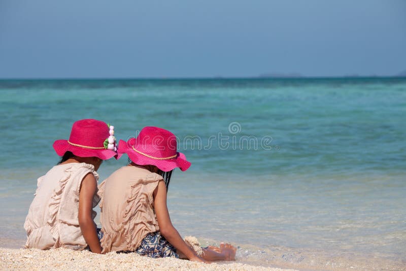 Zwei nette asiatische kleines Kindermädchen, die zusammen mit Sand auf dem Strand nahe dem schönen Meer sitzen und spielen stockfotos