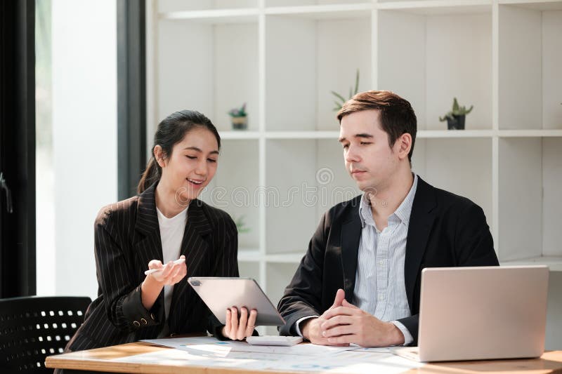 Zwei Personen sitzen an einem Schreibtisch mit Laptop und Tablet vor ihnen stockfoto
